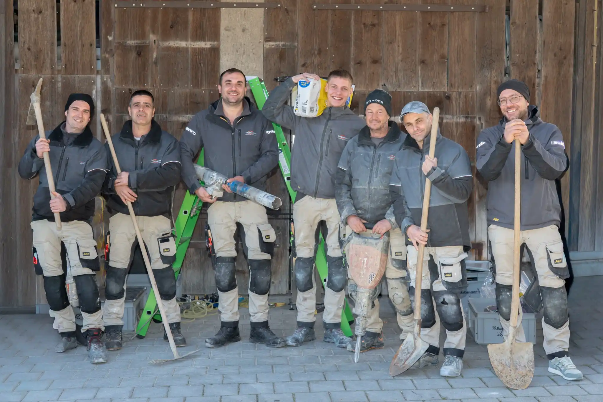 Teamfotografie in Männedorf: sieben Mitarbeiter eines Bauunternehmens mit Werkzeug vor einem Holztor