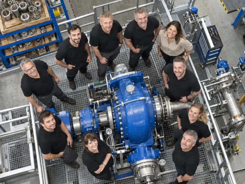 Unternehmensfotografie: Teamfoto von oben, zehn Mitarbeitende stehen in der Werkhalle um eine blaue Pumpanlage